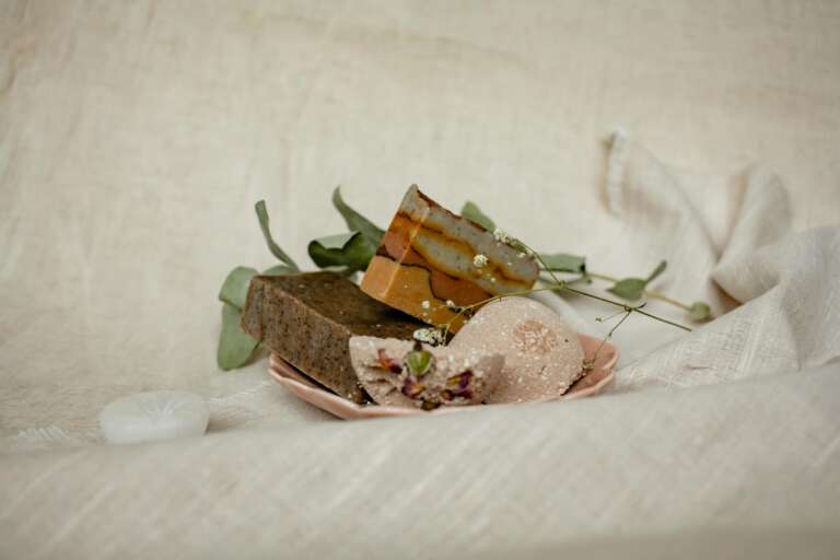 An artistic display of handmade soaps with natural leaves on a soft fabric background.