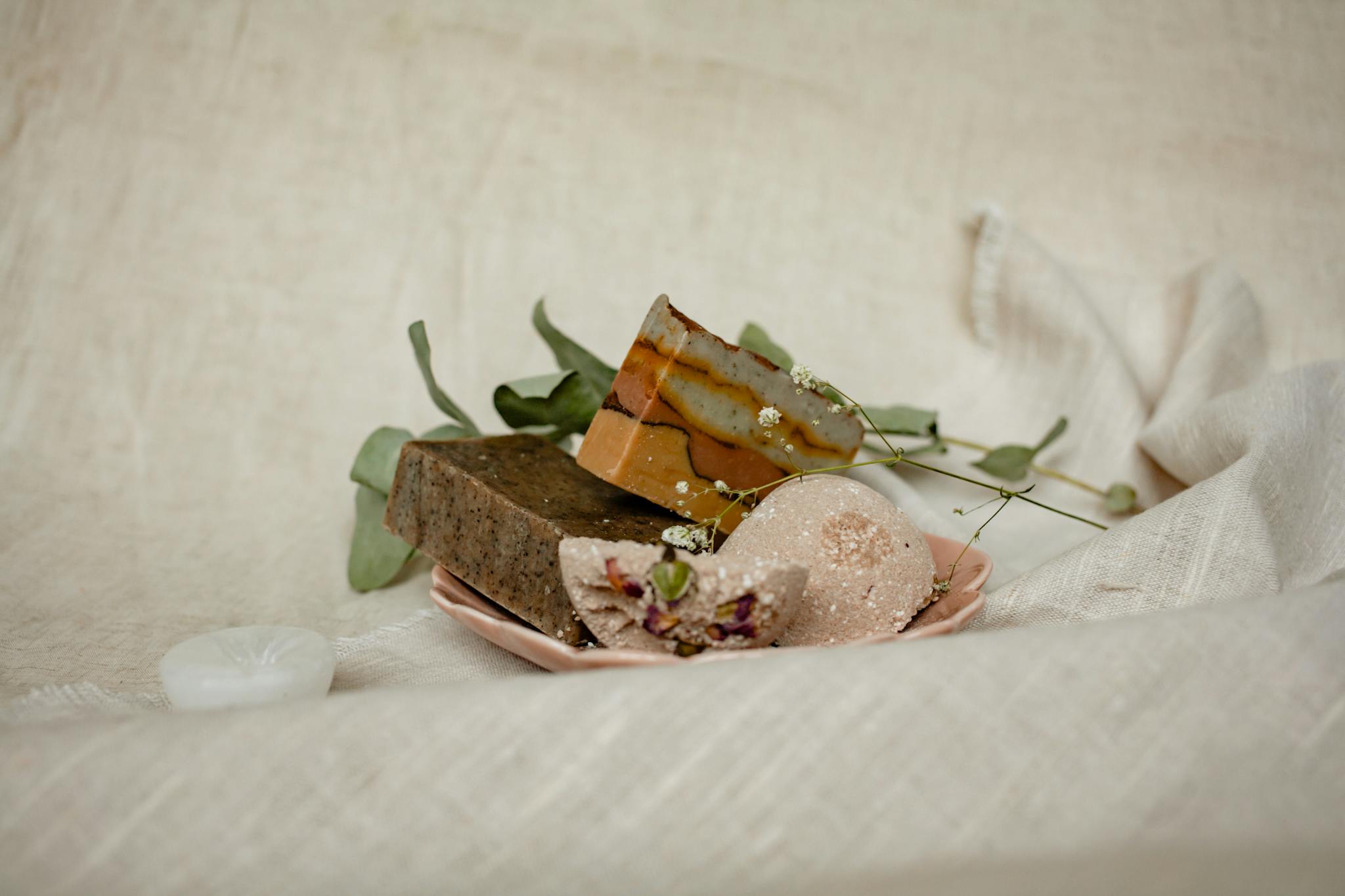 An artistic display of handmade soaps with natural leaves on a soft fabric background.