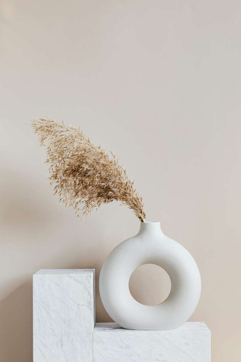 Elegant ceramic vase with dried grass on a marble pedestal, showcasing simplicity and minimalism.